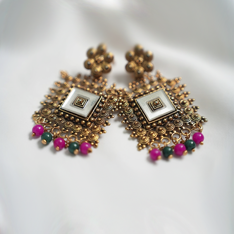 Antique Gold Toned Brass Jhumka Earrings With White Enamel Detail And Pink & Green Bead Drops